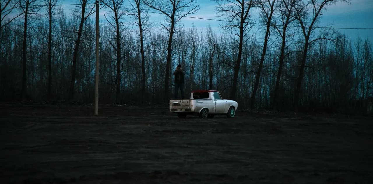 A white pickup truck parked on open ground in front of bare trees at dusk