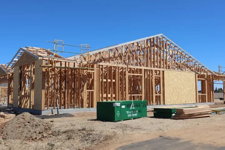 A timber-framed house under construction with lumber stacked beside it